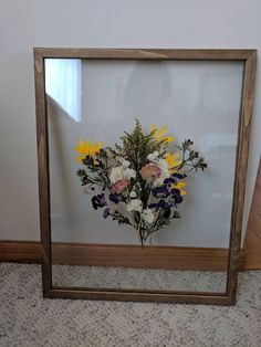 a wooden frame with flowers in it sitting on the floor next to a white wall