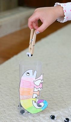 a child's hand holding a toothpick over a plastic cup with an animal drawn on it