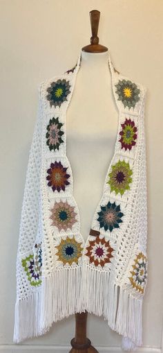 a white crocheted shawl with multicolored flowers and fringes on it