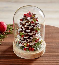 a snow globe with a pine cone and red berries in it on a wooden table