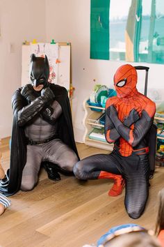 two children dressed up as batman and spider - man sitting on the floor in their bedroom