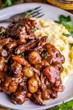 a white plate topped with meat covered in gravy next to mashed potatoes