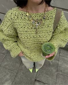 a woman holding a green cup in her hand and wearing a crochet sweater