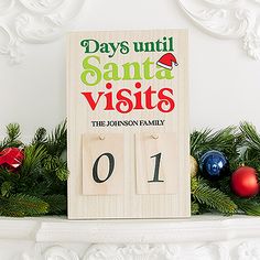 a wooden calendar sitting on top of a mantle next to christmas balls and greenery