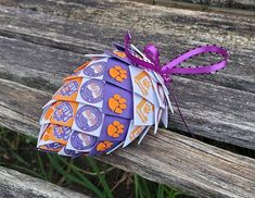 an origami ball sitting on top of a wooden bench next to a purple ribbon