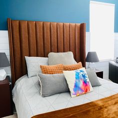 a bedroom with blue walls and brown leather headboard on the bed is decorated with colorful pillows