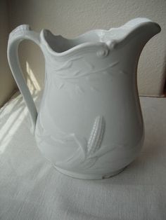 a white pitcher sitting on top of a table next to a window with sunlight coming through it