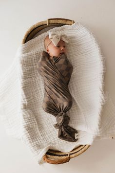 a baby wrapped in a blanket laying on top of a white blanket covered in brown checkered fabric