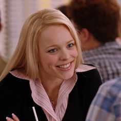 a woman sitting at a table with a pen in her hand and smiling for the camera