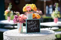 a table with flowers and a sign on it that says made flower market next to two vases