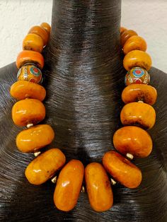 This exotic and wild Berber Style Moroccan Resin tribal statement necklace is an awesome piece for either a man or woman. These huge, bold and chunky Moroccan Resin beads have the look of the real organic amber without the price. The largest bead measures approximately 2" while the smallest measures approximately 1". Each has a shiny gold tone metal ball spacer. There are two Tibetan resin accent beads inlaid with brass, turquoise and coral. The back is finished with Chinese brass coins and ornate gold beads. Adjusts from 24-27" and I can add more links if requested. Gold tone hardware, lobster clasp and a 3" extender complete the piece. Stunning worn alone or layered copper, coral or turquoise. An ethnic, haute couture unisex piece from the Atelier of Kat Kouture. Has a strong street styl Luxury Bohemian Beaded Necklaces With Bead Caps, Luxury Artisan Beads For Festivals, Luxury Festival Jewelry With Round Beads, Luxury Artisan Round Beads, Luxury Round Beads Necklaces For Festivals, Luxury Unique Jewelry With Round Beads, Luxury Colorful Round Beaded Jewelry, Luxury Large Festival Beads, Luxury Orange Bohemian Necklace