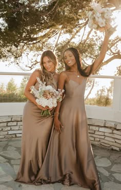 two women in brown dresses standing next to each other holding bouquets and smiling at the camera