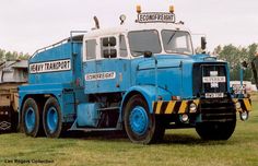 a large blue truck parked on top of a lush green field