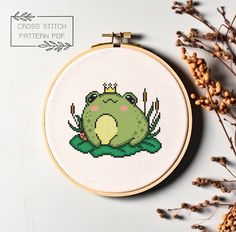 a cross stitch frog sitting on top of a plant