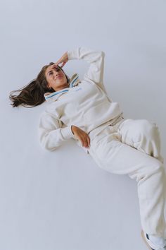 a woman laying on the ground with her arms behind her head, wearing a white sweatshirt and sweatpants