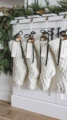 christmas stockings hanging from hooks in front of a mantle with evergreen garland and bells on it