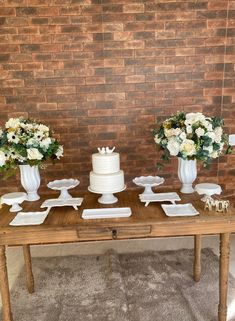 three white vases with flowers are sitting on a wooden table in front of a brick wall