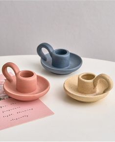 three ceramic cups and saucers sitting on top of a white table next to each other