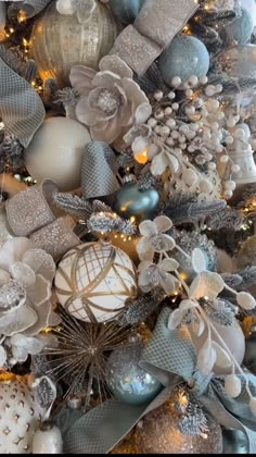 a christmas tree is decorated with silver and white balls, ornaments, and bows on it