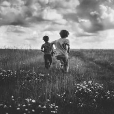 two young children running through a field with flowers in the foreground and clouds in the background