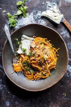 a plate of spaghetti with parmesan cheese and herbs on the side next to a fork