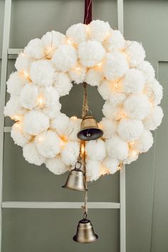 a christmas wreath hanging from a ladder with lights on it and bells attached to the front