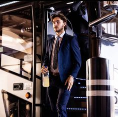 a man in a suit and tie standing next to a bus door holding a bottle