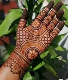 a woman's hand with henna on it and some plants in the background