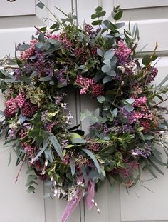 a wreath with purple flowers and greenery hangs on the front door to welcome guests