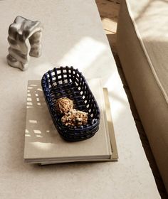 a basket sitting on top of a white table next to a book and vase with rocks in it