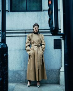 a woman standing in front of a building wearing a trench coat and heels with her hands on her hips