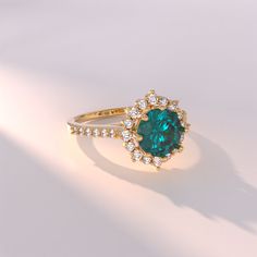 an emerald colored stone surrounded by white and yellow diamond accents on a gold band ring