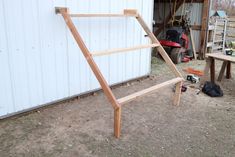 a wooden frame sitting in the dirt next to a white building with tools on it