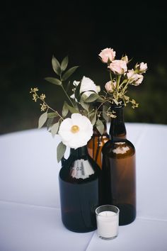 two bottles with flowers in them sitting on a table