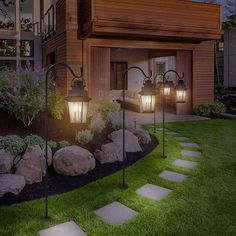 some lights that are on in front of a house with grass and rocks around it