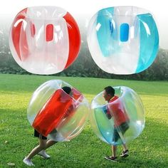 two people are playing with large inflatable balls on the grass, and one person is walking behind them