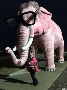 a woman standing next to an elephant statue with glasses on it's head and its trunk