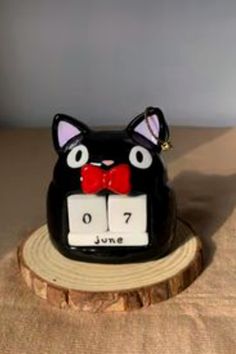 a black cat figurine sitting on top of a tree stump with a red bow tie