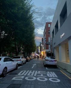 cars parked on the side of a street next to tall buildings and trees at dusk