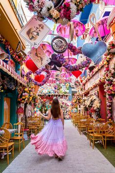 a woman in a pink dress is walking down the street with lots of decorations hanging from the ceiling