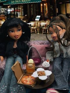 two dolls are sitting on a couch eating pizza