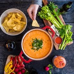 a person dipping tortilla chips into a bowl of red sauce and garnished with cilantro