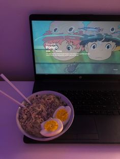 an open laptop computer sitting on top of a desk next to a bowl of noodles