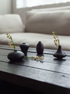 three black vases with flowers in them sitting on a wooden table next to a couch