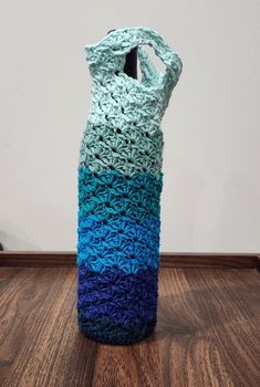 a crocheted blue and green bag sitting on top of a wooden floor next to a wall