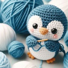 a crocheted penguin sitting next to balls of yarn