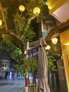 the umbrellas are hanging from the tree in front of the building with lanterns on it