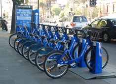 a row of blue bikes parked next to each other on a sidewalk near a parking meter