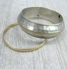 "A pair of matching Vintage brass bracelets in boho style, can be worn as a set or each one separately. These bracelets were a travel souvenir from India, made in the 1980s. Wide bracelet: silver plated brass, 14 mm wide and 6-7 mm thick with textured hammered surface and a rib around the middle. The silver plate is a bit worn off, the edges and the rib looks gold color. Narrow bracelet: 6 mm wide, gold plated brass with textured surface, the pattern looks like flowers and leaves. Length: 8 inch Bohemian Stackable Metal Bangle, Bohemian Hammered Brass Bracelets, Bohemian Gold Hammered Bracelets, Festival Brass Bracelets In Silver Color, Silver Hammered Bohemian Bracelets, Silver Brass Bracelets For Festival, Bohemian Hammered Metal Bracelets, Hammered Silver Brass Bracelets, Silver Hammered Brass Bracelets