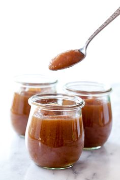 three jars filled with peanut butter on top of a marble counter next to a spoon